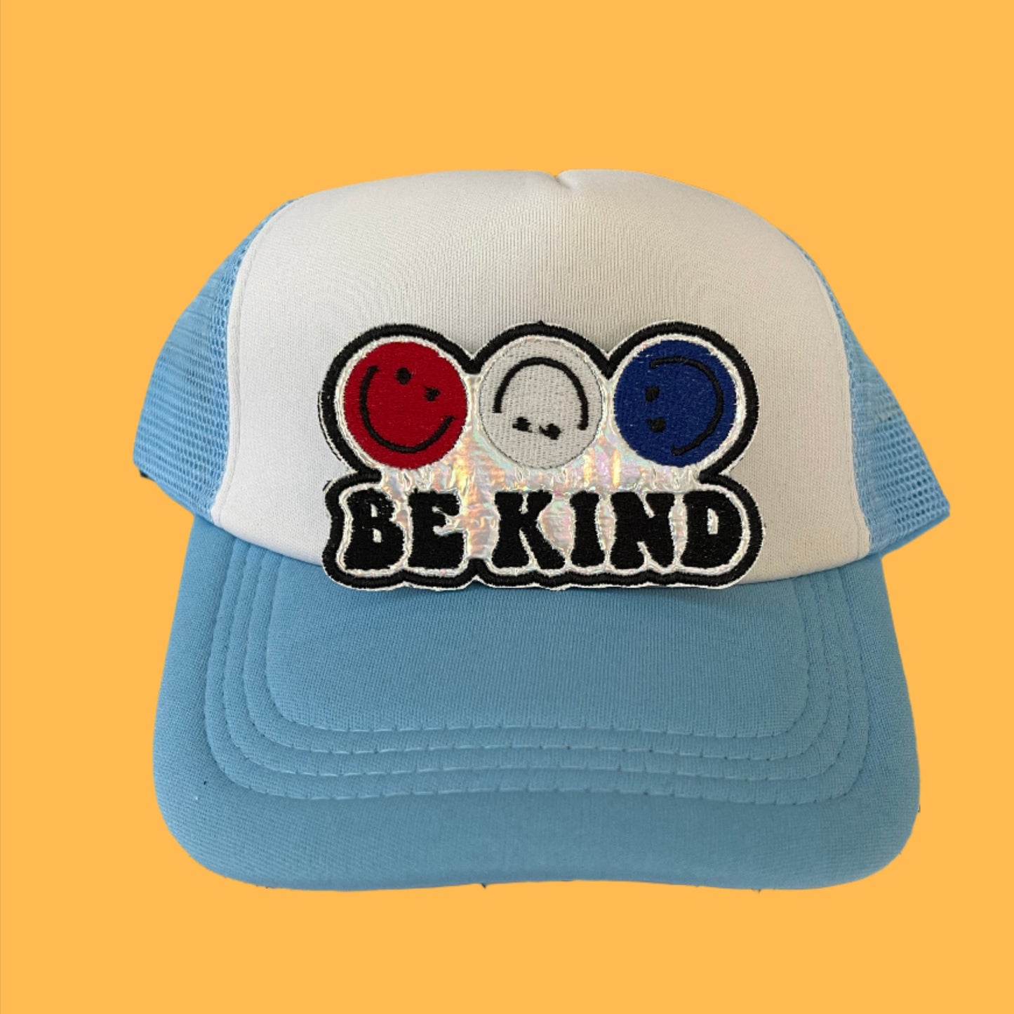 Iron-on patch featuring three smiley faces in red, white, and blue with the phrase "BE KIND" on a holographic silver background.