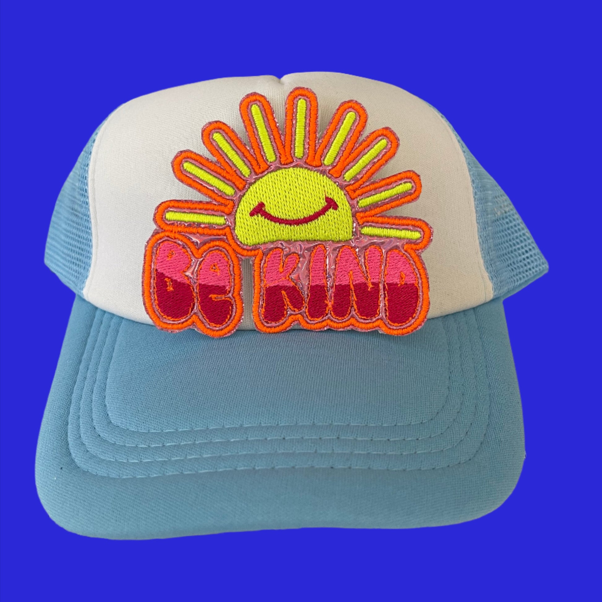Iron-on patch featuring a cheerful sun with a smiling face, embroidered in bright yellow and outlined in neon orange, with the phrase "BE KIND" in two-tone pink and outlined in neon orange.