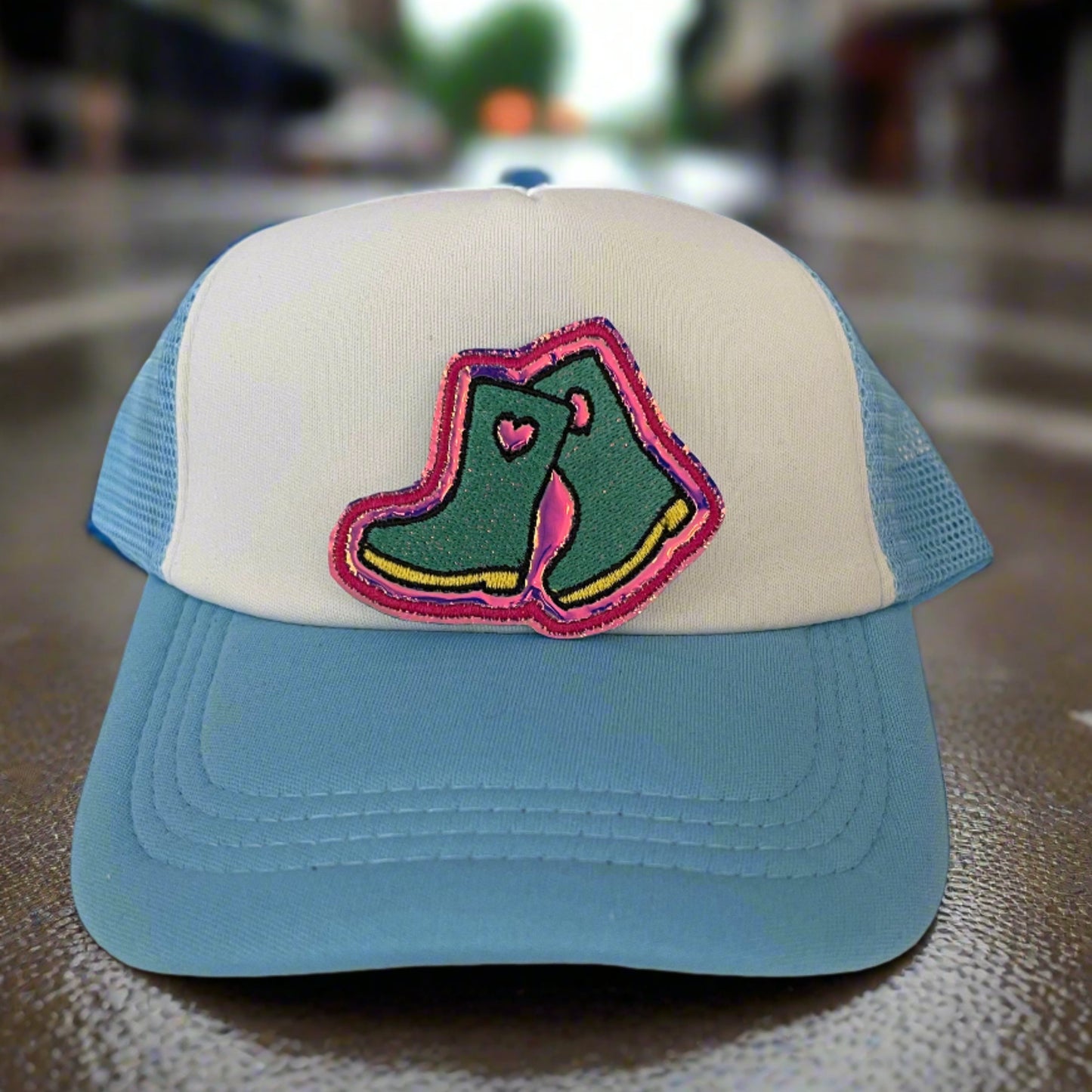 Close-up of a quirky rain boots embroidered patch with green and pink detailing, perfect for customizing hats and other accessories.