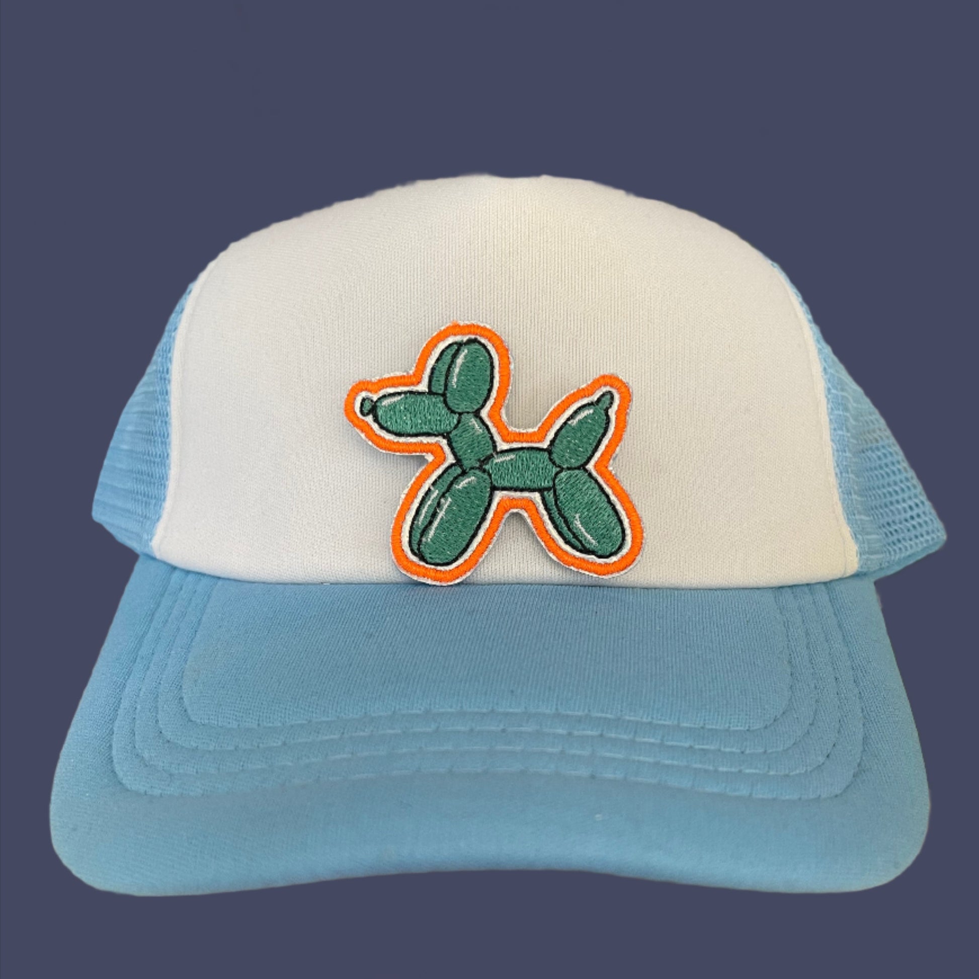 Close-up of a playful balloon dog patch on a hat, featuring vibrant green and orange colors.