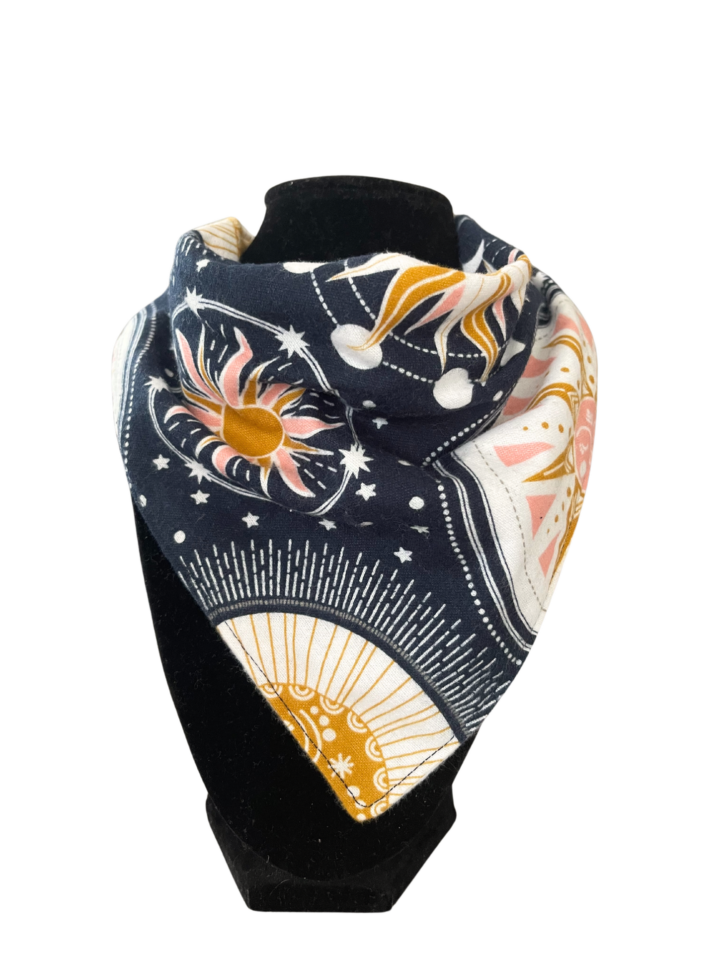 Reversible bib-dana with a celestial pattern featuring sun, moon, and stars in navy, yellow, pink, and white on one side and solid color cotton flannel on the reverse, displayed on a black mannequin.