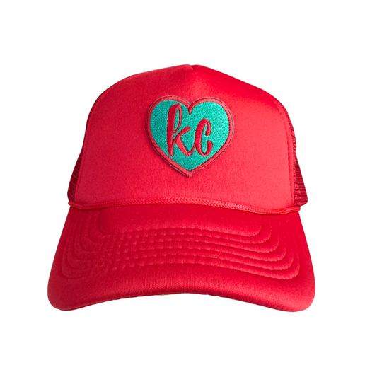 Heart-shaped "KC" patch in teal on a red KC Current hat.

