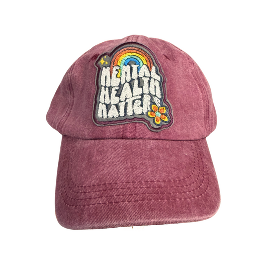 "Mental Health Matters" embroidered patch with rainbow on a mauve hat.

