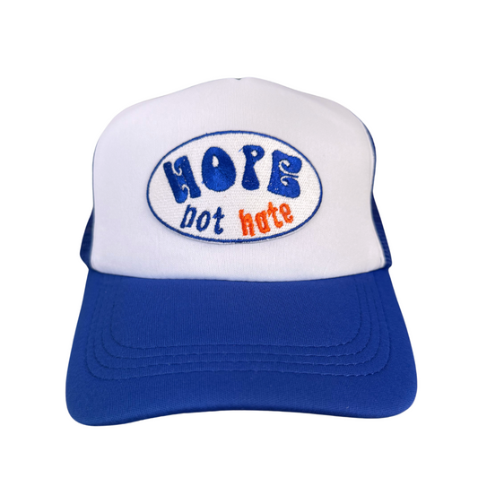 Front view of a blue and white trucker hat featuring an embroidered "Hope Not Hate" patch in blue and orange.

