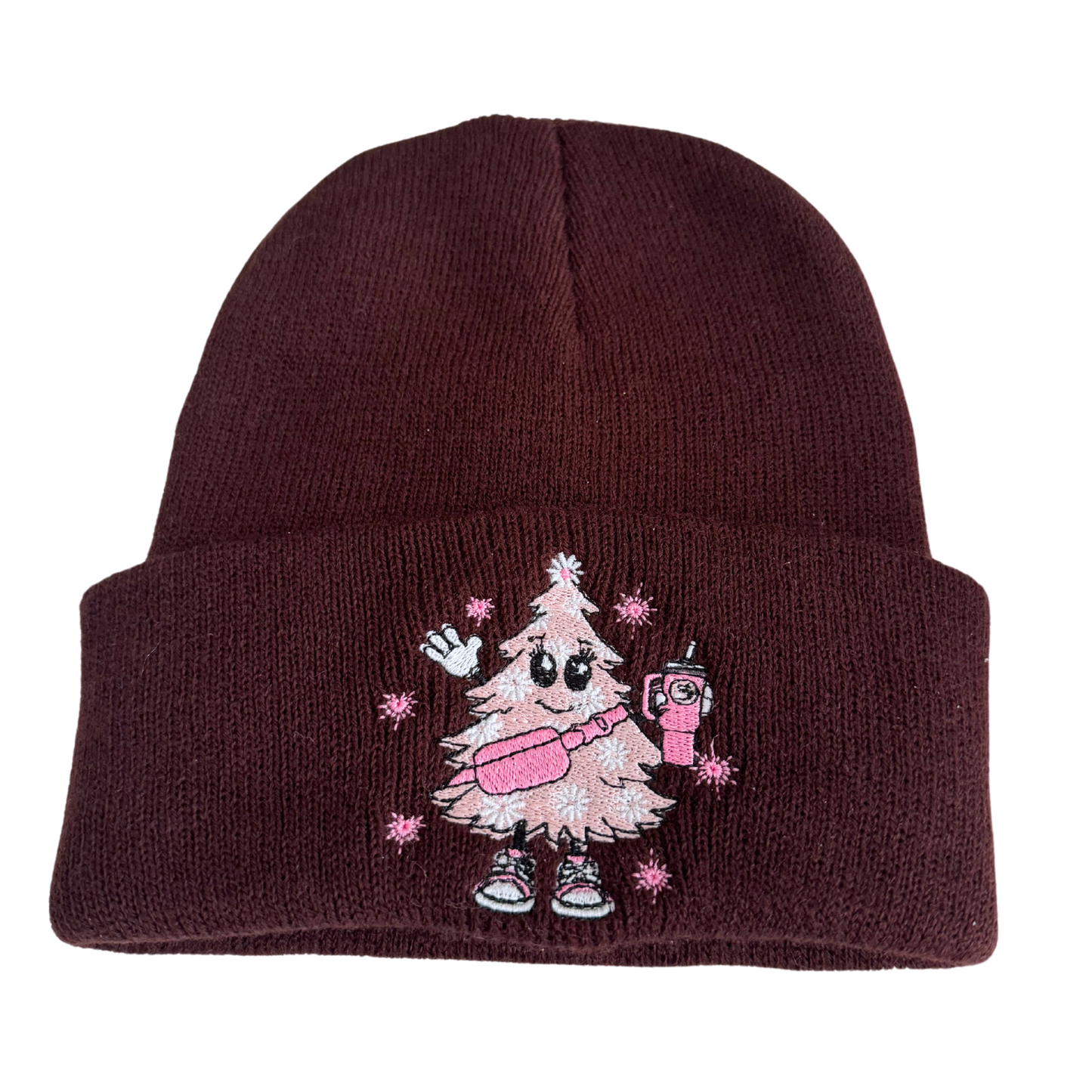 Brown beanie with a pink Christmas tree embroidery wearing sneakers and holding a festive drink.

