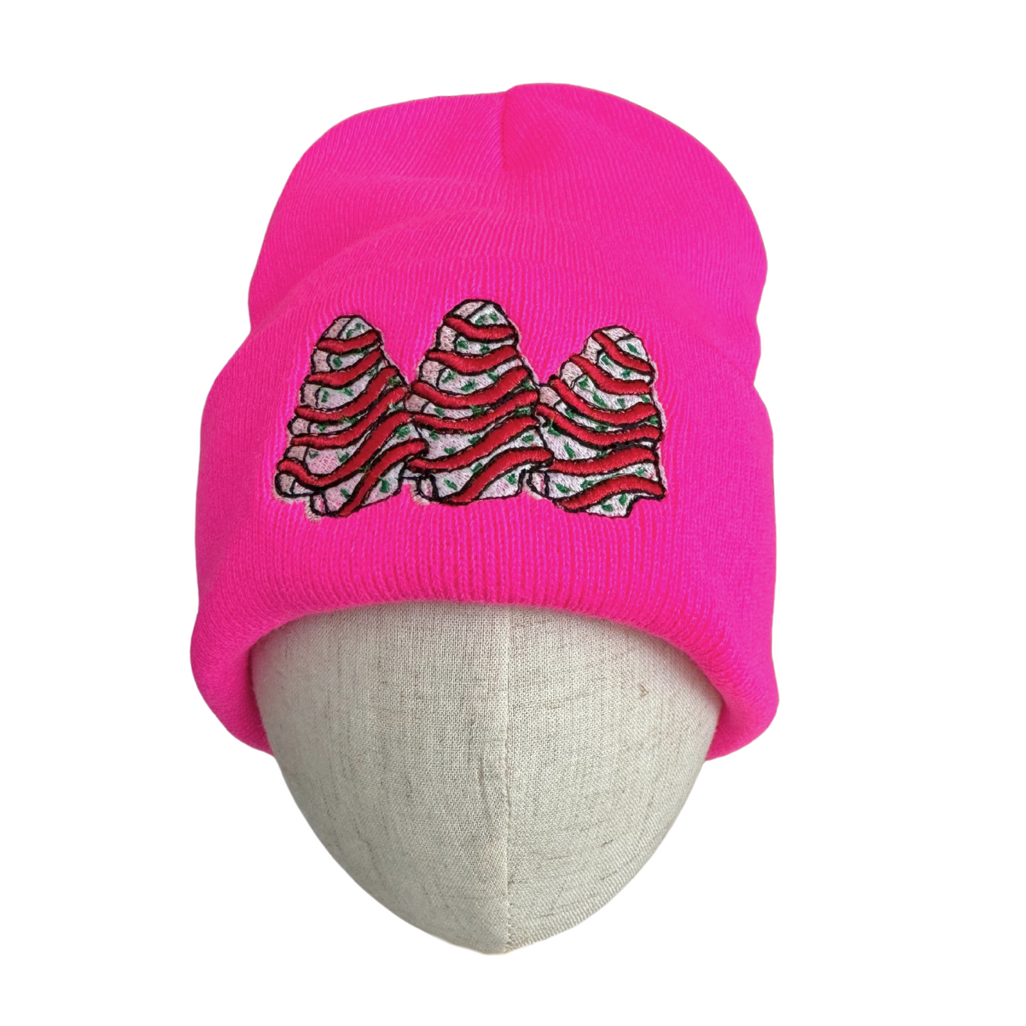 Bright pink beanie with embroidered Christmas tree snack cake design

