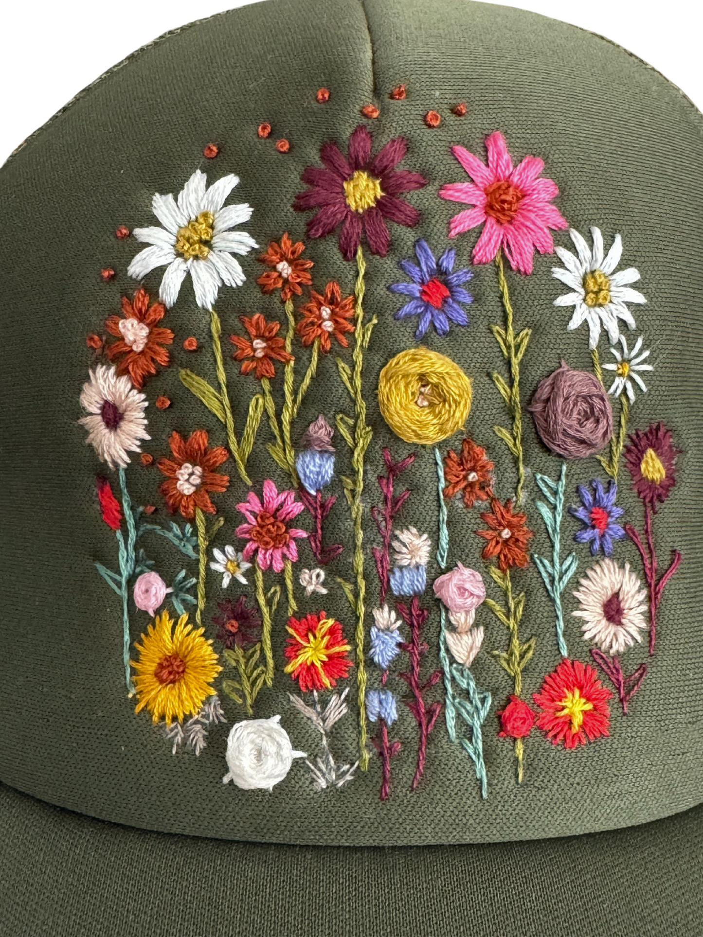 Close-up of hand-embroidered wildflower field design on an olive green trucker hat.

