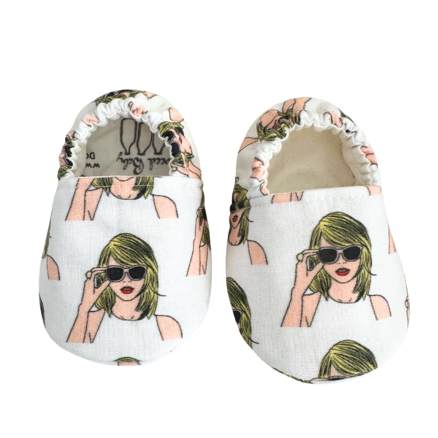 Close-up of baby moccasins featuring a Taylor Swift-inspired print with blonde hair, sunglasses, and a white tank top, handmade with vegan materials and elastic backs for a secure fit, size 0-3 months.

