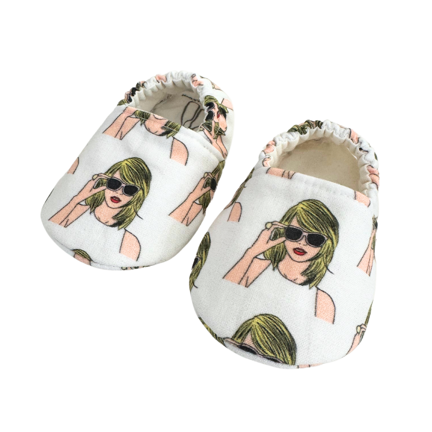 Close-up of baby moccasins featuring a Taylor Swift-inspired print with blonde hair, sunglasses, and a white tank top, handmade with vegan materials and elastic backs for a secure fit, size 0-3 months.

