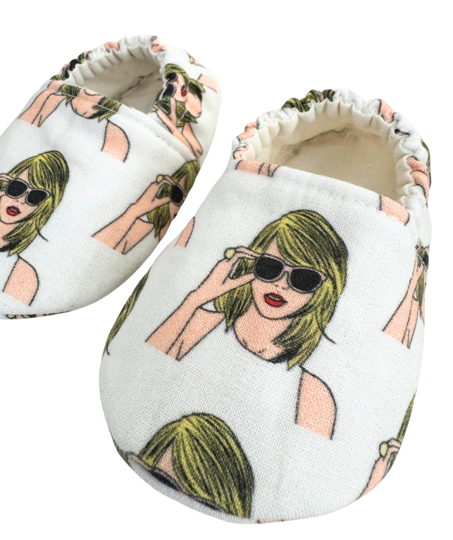 Close-up of baby moccasins featuring a Taylor Swift-inspired print with blonde hair, sunglasses, and a white tank top, handmade with vegan materials and elastic backs for a secure fit, size 0-3 months.

