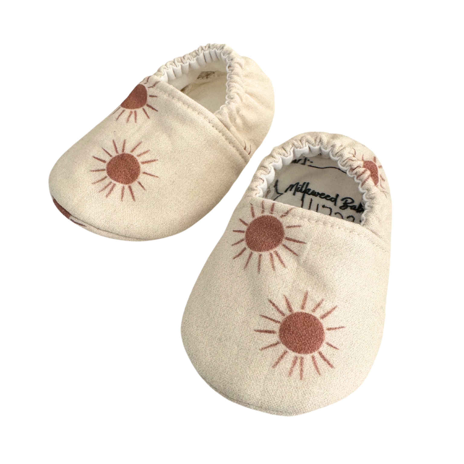 Baby moccasins with a neutral beige base featuring rust-colored sunburst prints, handmade with vegan materials and an elastic back for a snug fit, size 0-3 months, ready to ship.

