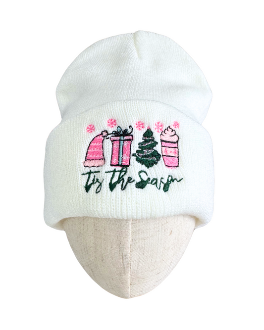 White beanie with "Tis The Season" festive embroidery featuring a pink hat, gift box, Christmas tree, and hot cocoa cup.

