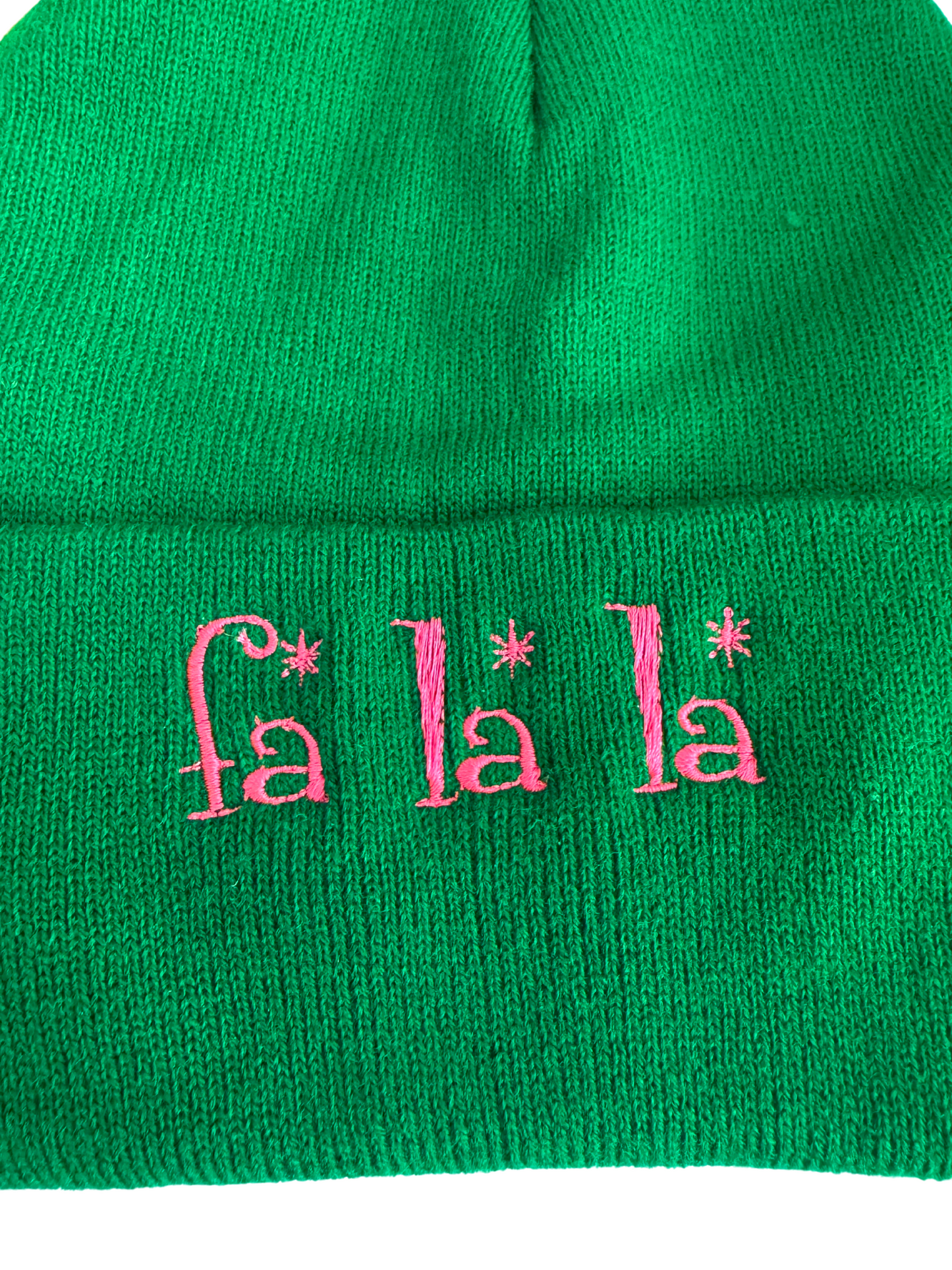 Green beanie with pink "Fa La La" embroidered text, festive winter holiday theme.

