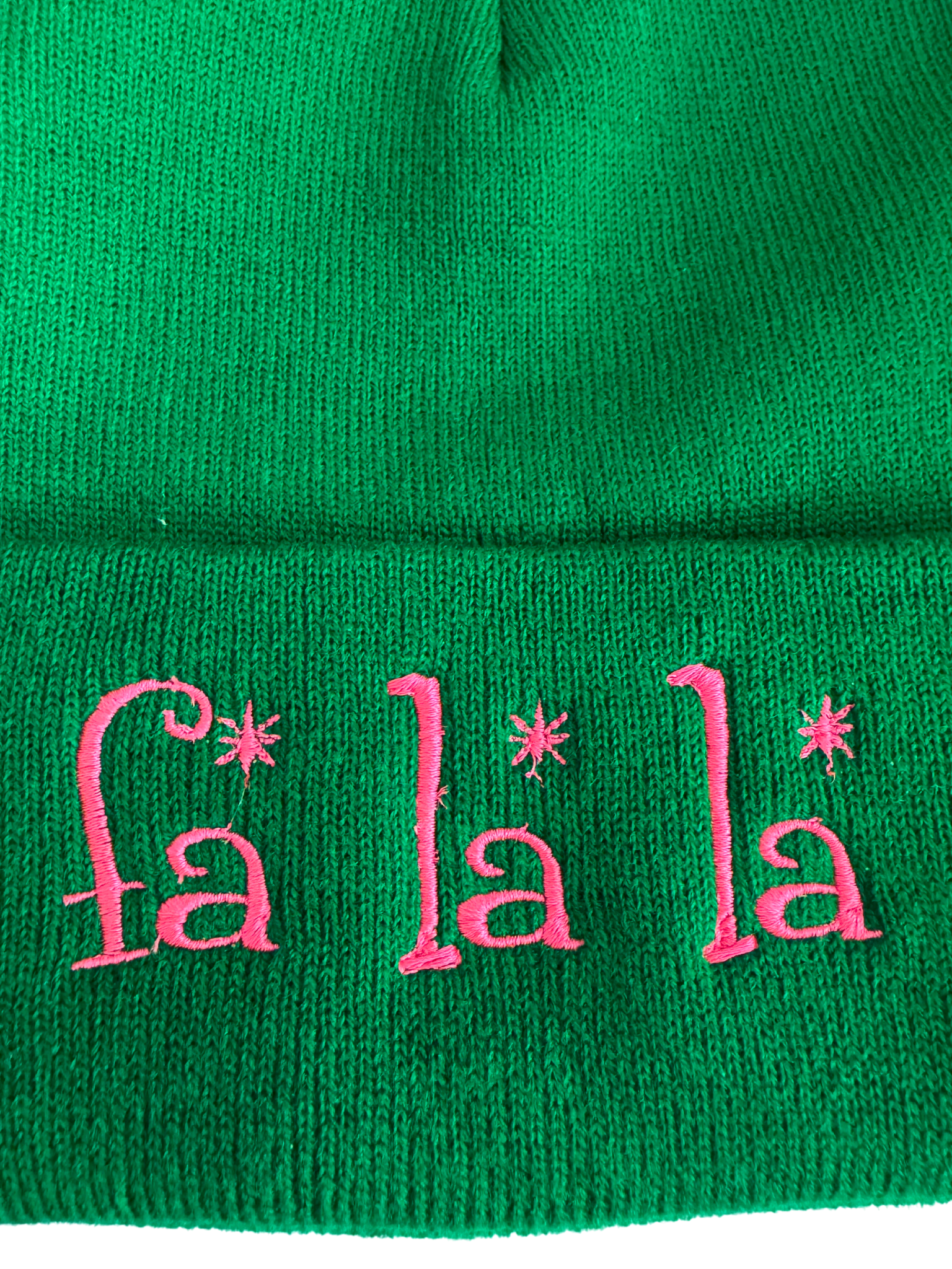 Green beanie with pink embroidered "Fa La La" design featuring whimsical fonts and festive charm.

