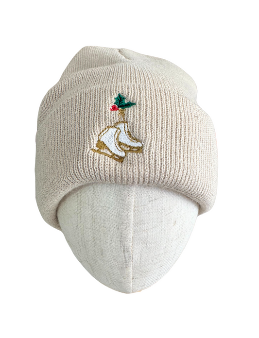 Beige knit beanie with embroidered golden ice skates and holly design.

