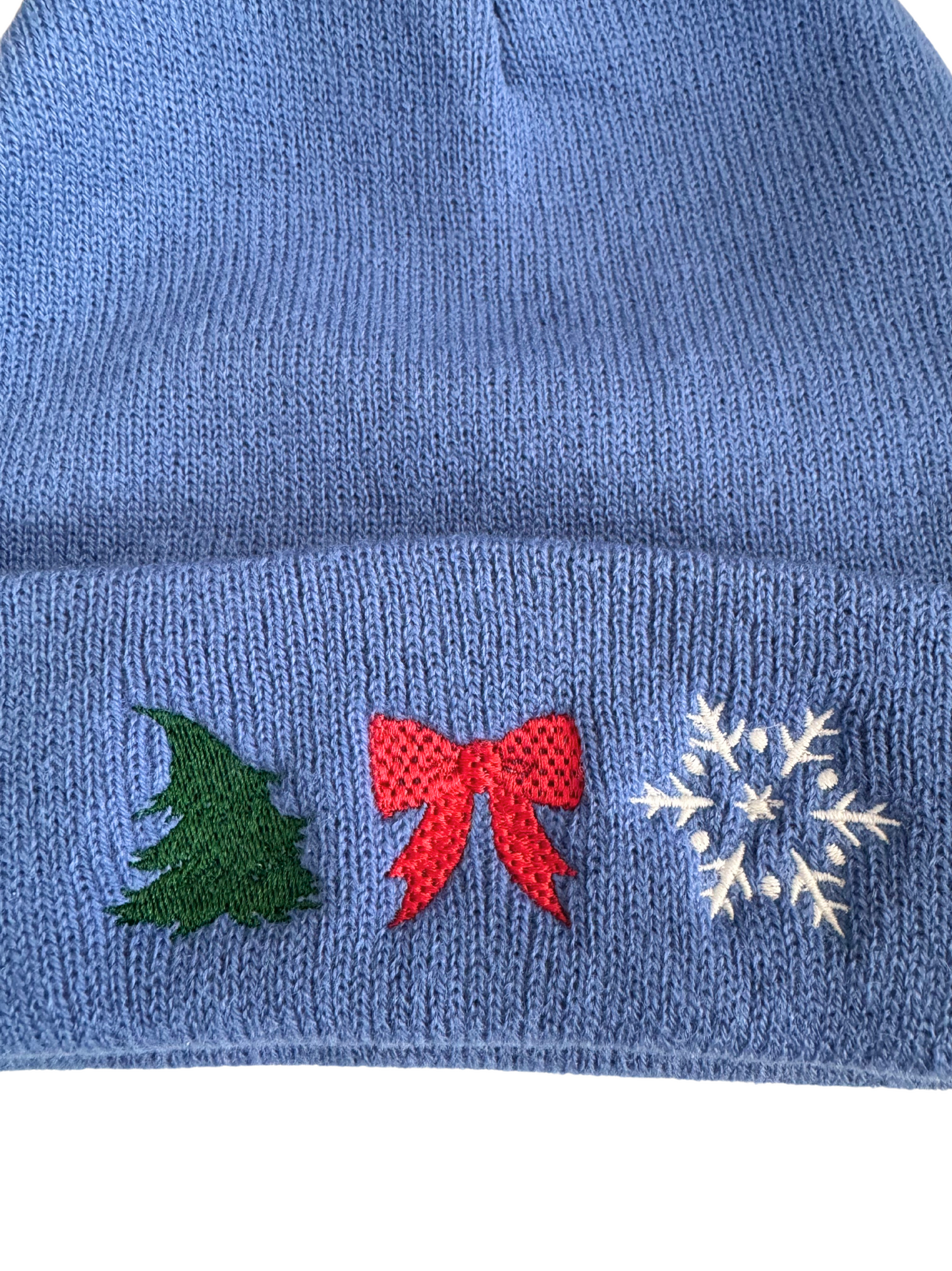 Blue holiday beanie with machine-embroidered Christmas tree, red bow, and snowflake designs.

