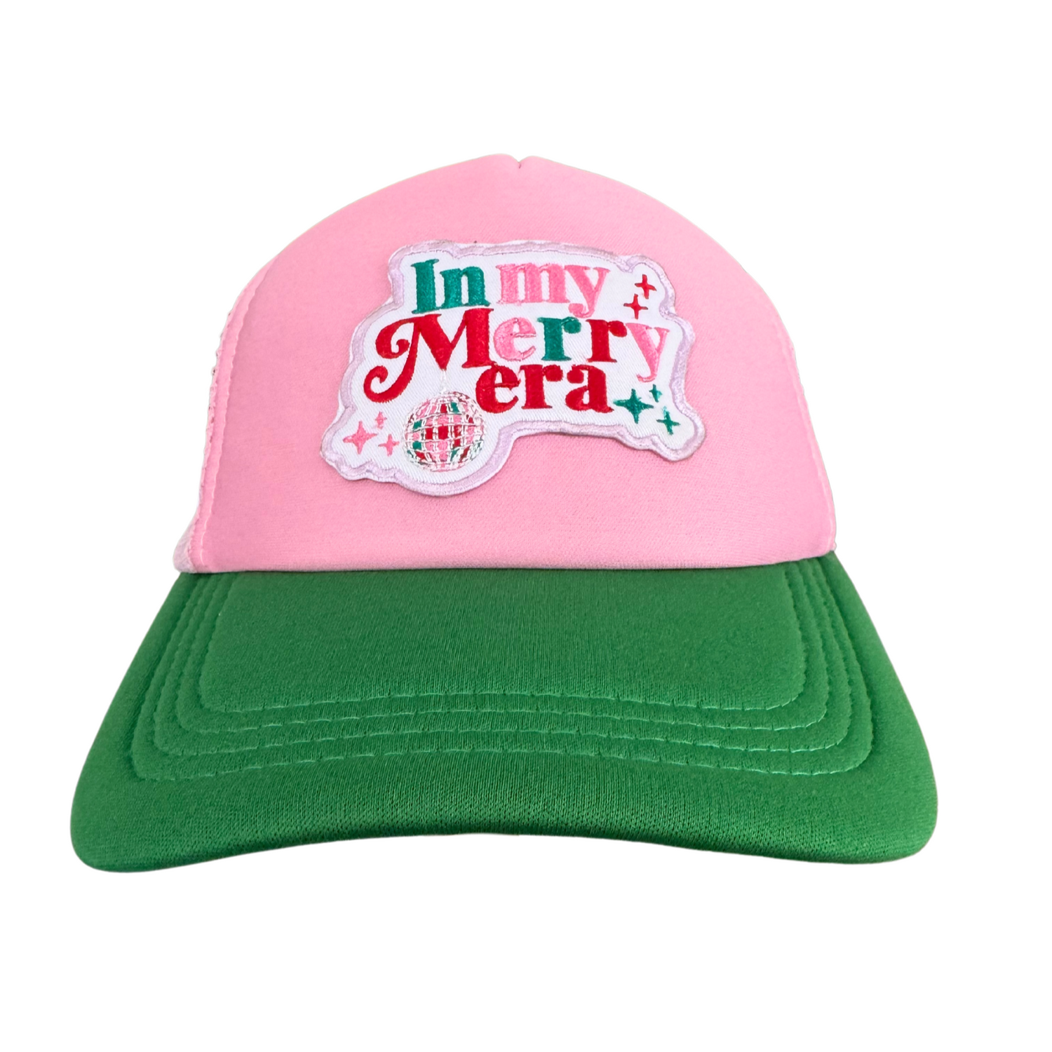 Pink and green trucker hat featuring an embroidered "In My Merry Era" patch with a disco ball and holiday-themed accents.

