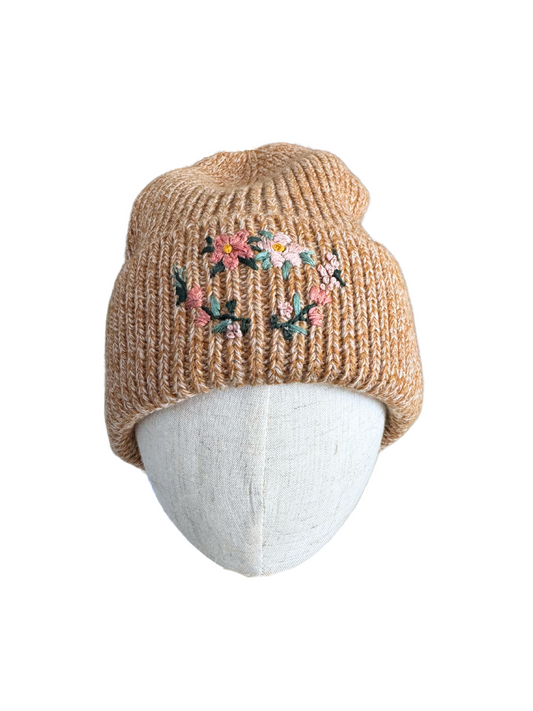 Golden knit beanie featuring a detailed hand-embroidered floral wreath with pink flowers and greenery.
