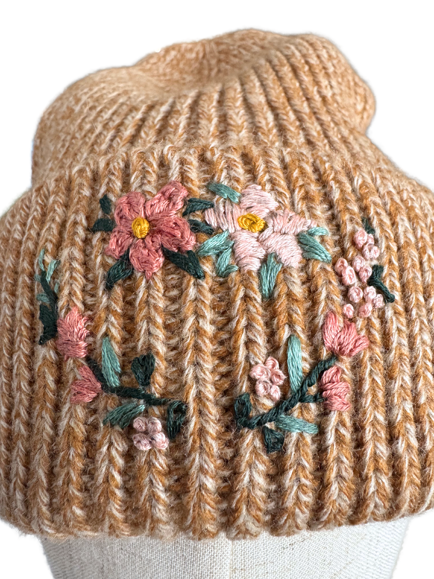 Close-up of hand-embroidered floral wreath design on golden knit beanie, highlighting craftsmanship.
