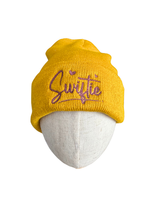 Mustard yellow beanie with purple "Swiftie" embroidery.

