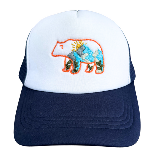 Hand-stitched trucker hat with embroidered bear and mountain design.