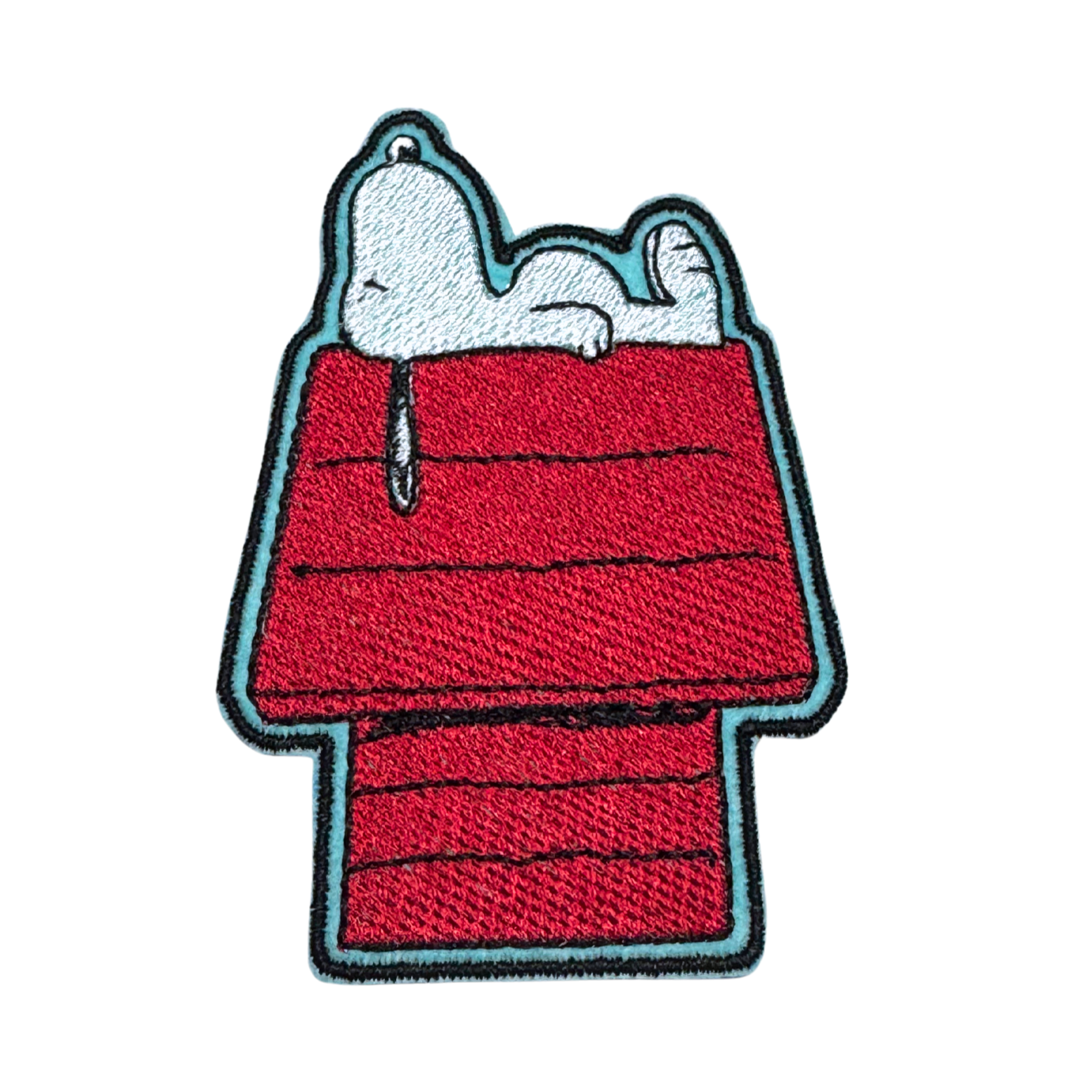 Embroidered patch featuring a relaxed white dog lounging on top of a red doghouse.
