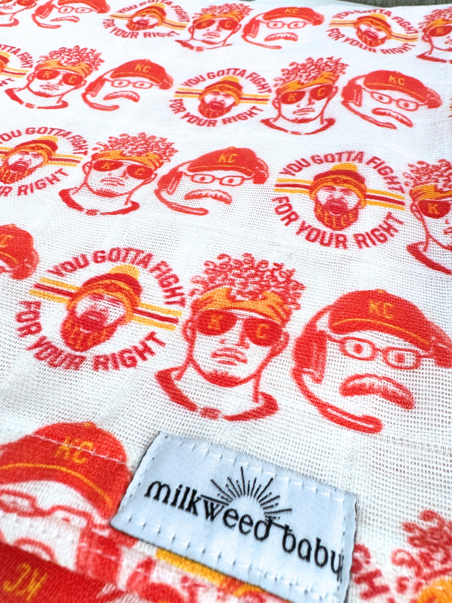 Close-up of a KC Chiefs-inspired baby swaddle blanket featuring illustrations of Patrick Mahomes, Travis Kelce, and Andy Reid with the slogan "You Gotta Fight for Your Right" in red and yellow, printed on organic muslin gauze.