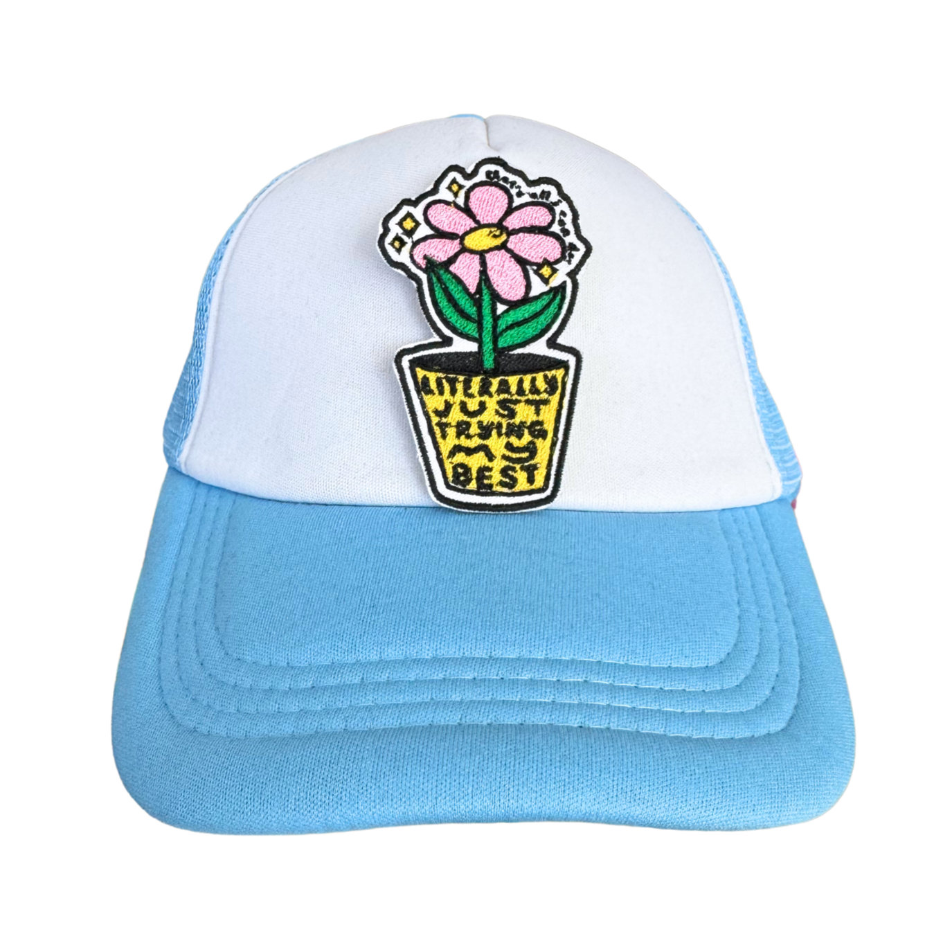 A trucker hat with a white front panel and light blue brim, featuring the "Literally Just Trying My Best" embroidered patch attached to the front.
