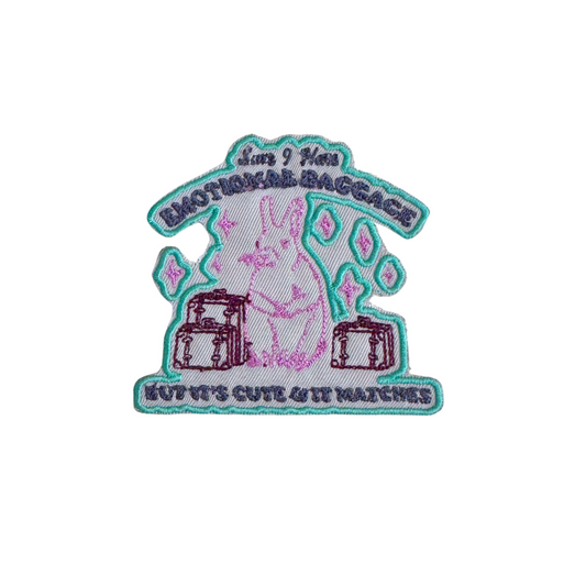 Embroidered patch featuring a bunny with luggage and the phrase "Sure, I Have Emotional Baggage, But It's Cute & It Matches," on a light background with teal and pink embroidery.
