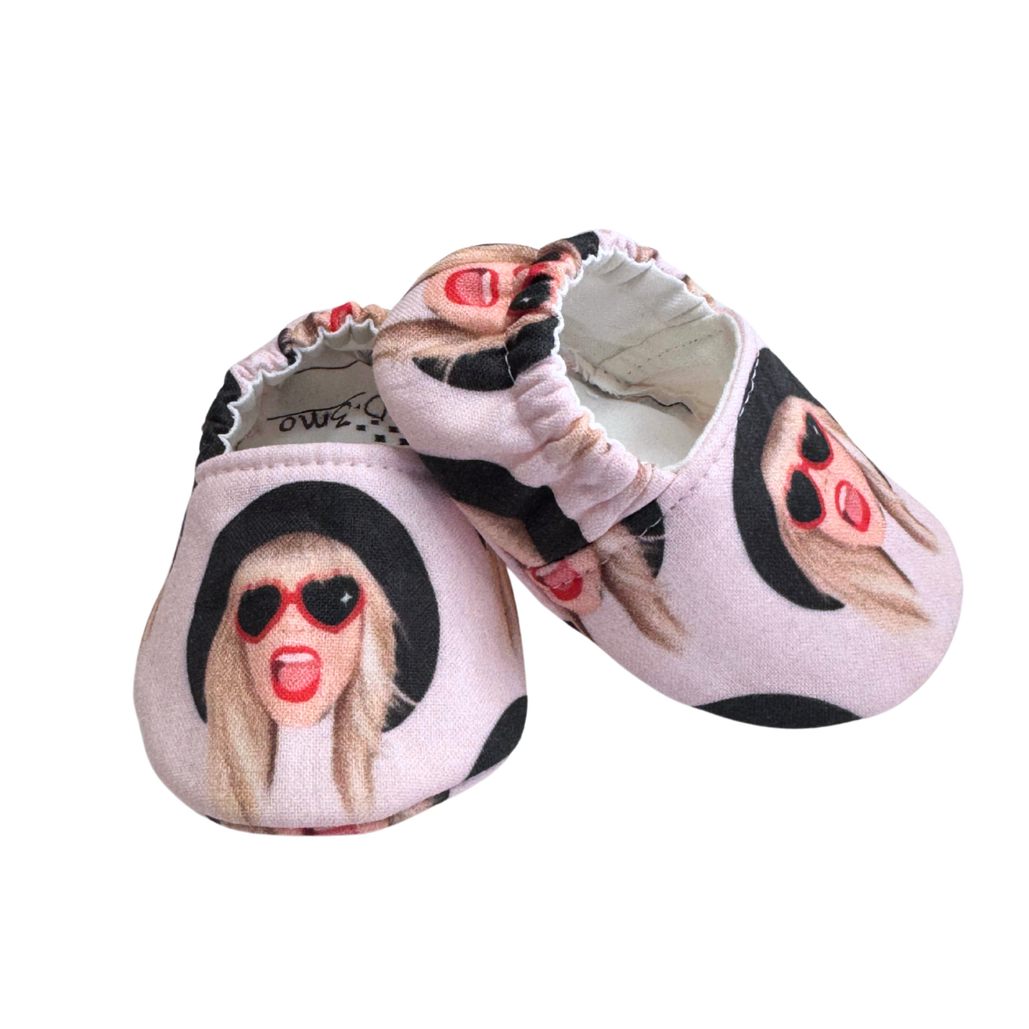 Side view of Taylor Swift baby moccasins, showing a fun pop culture design, soft soles, and a stay-on elastic back.