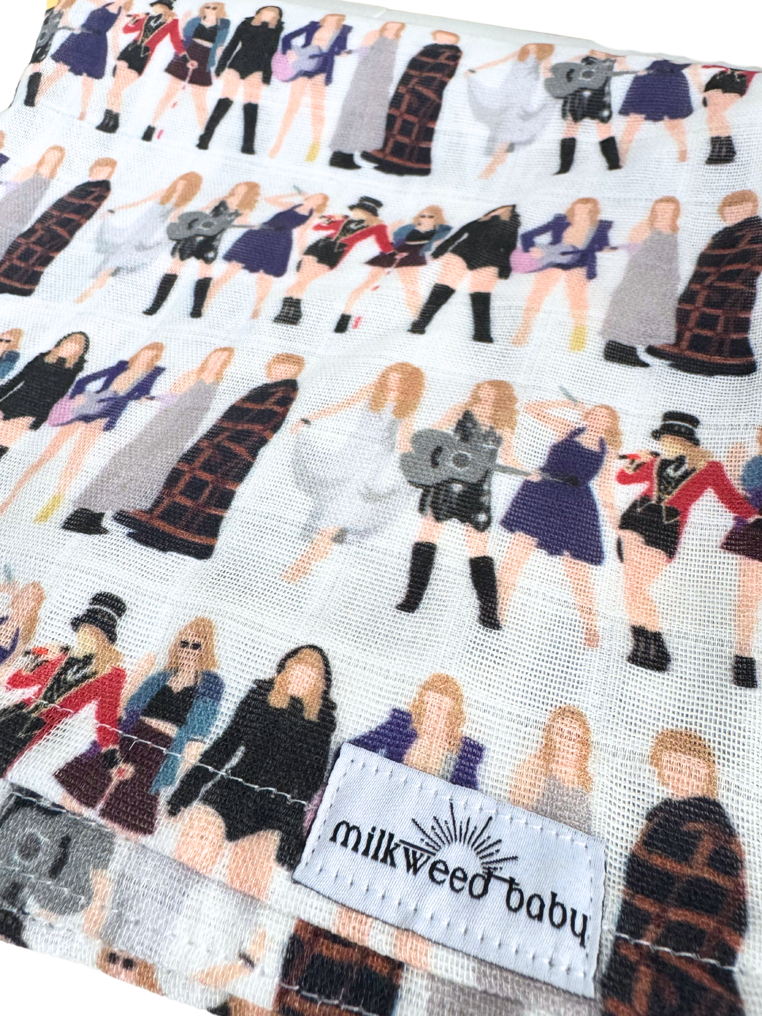 Close-up of a Taylor Swift Eras Tour baby swaddle blanket featuring a repeating pattern of iconic tour outfits from different eras, printed on soft, breathable organic muslin gauze with a "Milkweed Baby" tag.