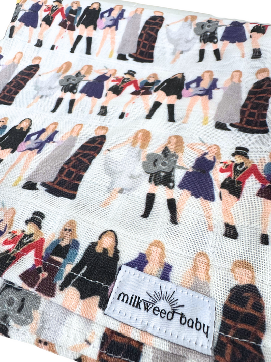 Close-up of a Taylor Swift Eras Tour baby swaddle blanket featuring a repeating pattern of iconic tour outfits from different eras, printed on soft, breathable organic muslin gauze with a "Milkweed Baby" tag.